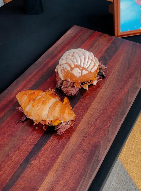 Concha and croissant barbecue sandwiches on a wooden board